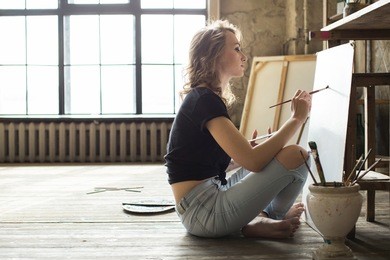 female artist working on painting in studio in front of an empty canvas in bright daylight studio