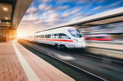 white modern high speed train in motion on railway station at sunset. train on railroad track with motion blur effect in europe in evening. railway platform. industrial landscape. railway tourism