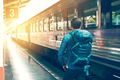 behind asian young man standing and waiting train on platform.