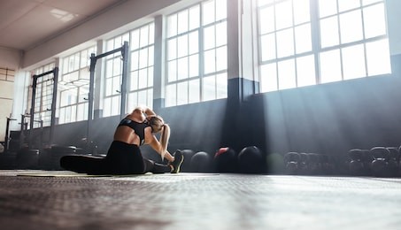 young woman working out in gym. back view of woman doing stretching exercise in the morning sunlight at the gym.
