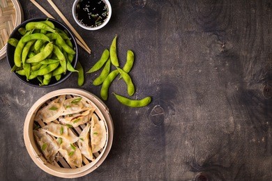 chinese dumplings in rustic wooden bamboo steamer with green boiled soybeans edamame, soy sauce and chopsticks. traditional chinese/asian dish. space for text. food background. dim sum dumplings