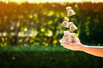 women hands hold a money bags and dropping on the top in the public park for loans to planned investment in the future concept.