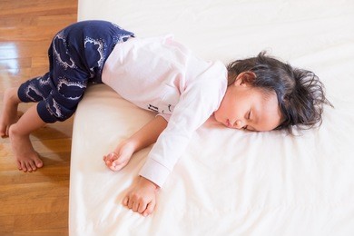 cute asian little girl is still sleeping in the morning time and her legs stabilize her body to prevent falling from the bed.