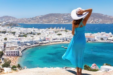attractive woman with blue dress enjoys the view over the town of mykonos, greece