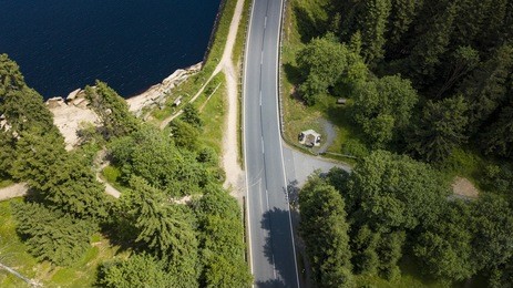 drone photography with a street crossing the harz national park at the edge of a mountain lake surrounded by fir trees.