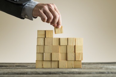 businessman building a structure with wooden cubes on table surface on sepia toned background, concept with copy space.