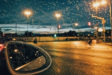 rain drops on car window with road light bokeh, city life in night in rainy season abstract background,water drop on the glass, night storm raining car driving concept.