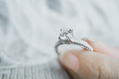  close up of woman's  hand holding elegant diamond ring with feather and gray scarf background. diamond ring.