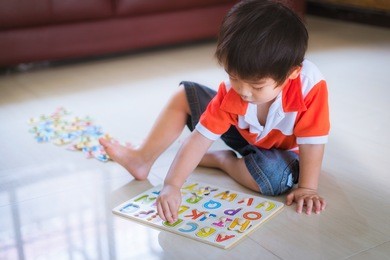 asian little boy playing with wooden letter puzzle sitting on the floor at home, early education and leaning.