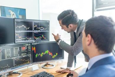 businessmen trading stocks online. stock brokers looking at graphs, indexes and numbers on multiple computer screens. colleagues in discussion in traders office. business success concept.