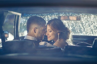 portrait of happy newlywed couple in car on sunset after rain