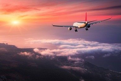 airplane. landscape with big white passenger airplane is flying in the red sky over the clouds at colorful sunset. journey. passenger aircraft is landing at dusk. business trip. commercial plane