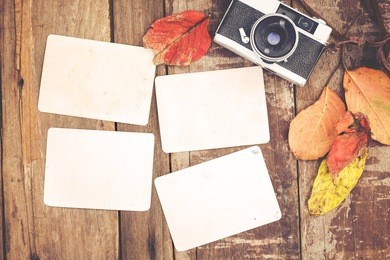 retro camera and empty old instant paper photo album on wood table with maple leaves in autumn border design - concept of remembrance and nostalgia in fall season. vintage rustic style.