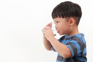 cute little asian boy drinking water from glass on white background