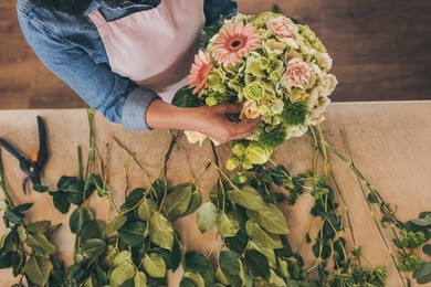 close-up partial view of young woman in apron working with bouquet of beautiful fresh flowers 