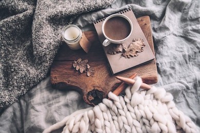 cup of coffee and candle on rustic wooden serving tray in the cozy bed with blanket. knitting warm woolen sweater in the autumn weekend, top view.