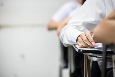 soft focus.university or high school student holding pencil.sitting on row chair writing final exam in examination room or study in classroom.student in uniform.education concept