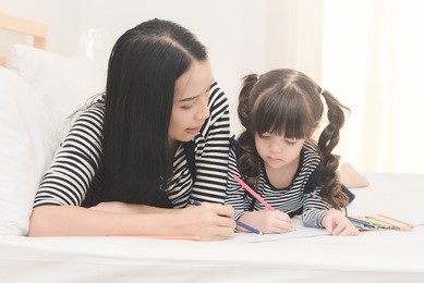 happy family in the bedroom,yong mother teaching her daughter child to studying at home.photo series of family, kids and happy people concept.