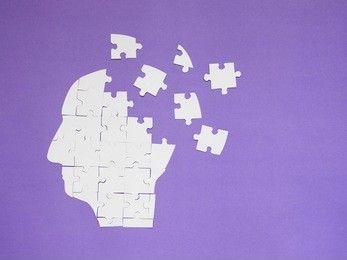 white jigsaw puzzle as a human brain on purple background w/ copy space. creative idea for memory loss, alzheimer's disease, dementia, parkinson's disease, emotion stress and mental health concept.