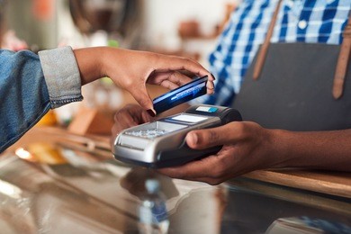 closeup of a customer using her credit card and nfs technology to pay a barista for her purchase at a cafe