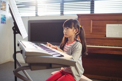 concentrated girl looking at notes while practicing piano in music class