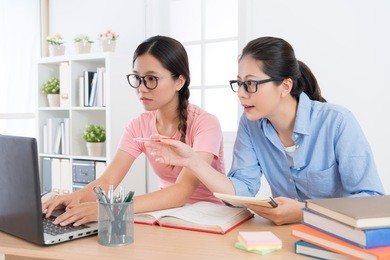 seriously pretty female college student using mobile laptop studying with her home tutor and researching school education homework answer through online e-learning system.