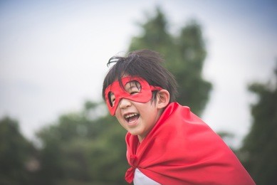 asian child in in superhero's costume playing in the park