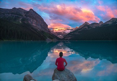 a man in red sit on rock watching lake louise in the morning sun light with colorful clouds and reflections
