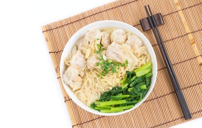 wonton and egg noodle soup of chinese cantonese style for asian cuisine serving with chinese cabbage (bog choy) and topped over bamboo plate mat isolated on white background, flat lay (top view)