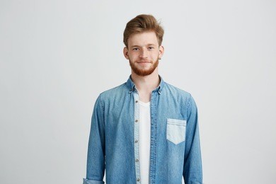 portrait of young handsome man in jean shirt smiling looking at camera over white background.