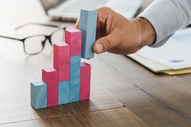 businessman working at office desk, he is building a growing financial graph using wooden toy blocks: successful business concept