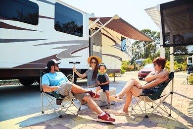 mother,father,son and grandmother sitting near camping trailer,smiling.woman,men,kid relaxing on chairs near car.family spending time together on vacation in modern rv park