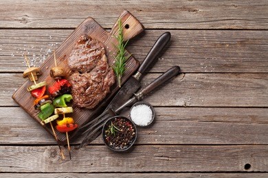grilled vegetables and beef steak on cutting board on wooden table. top view with copy space