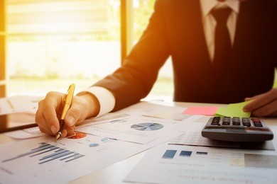 young business man holding pen pointing graph data documents working at office with tablet,calculator,post it note and    for  plans to improve quality next month on his desk.