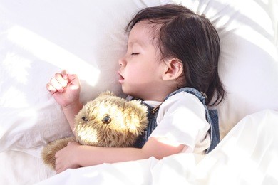 little asian girl sleeping in her bed and hugs a teddy bear