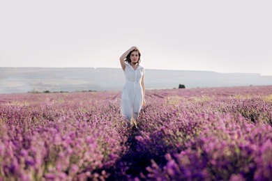 beautiful young woman walking in the lavender field. the girl is relaxing outside.
