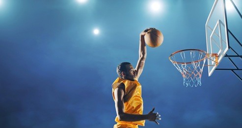 close up image of professional basketball player making slam dunk during basketball game in floodlight basketball court. the player is wearing unbranded sport clothes.
