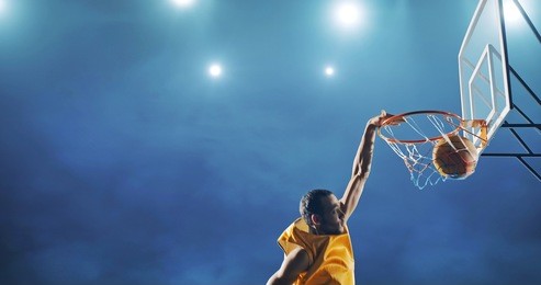 close up image of professional basketball player making slam dunk during basketball game in floodlight basketball court. the player is wearing unbranded sport clothes.