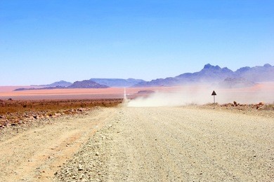 dust clouds at dry gravel road, driving offroad at dirt track in namib desert, namibia, africa