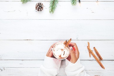 christmas background - girl hand holding cup of hot chocolate on white table with rustic decoration and copy space, flat lay, top view. vintage color tone style.