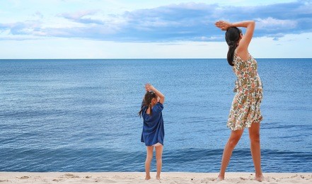 happy family. beautiful mother and her child girl doing yoga exercises on beach.