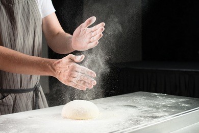 woman baker sprinkled flour on roll dough on a wooden board. process of preparing pizza. cooking time, cooking concept, selective focus