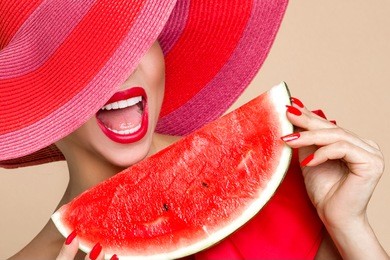 beautiful female model with perfect face and red hat holding a watermelon at her face