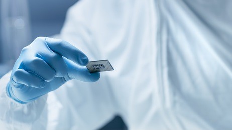 in ultra modern electronic manufacturing factory design engineer in sterile coverall holds microchip with gloves and examines it.