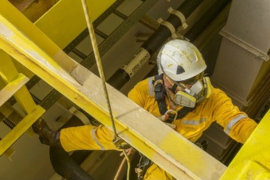 working at height. a commercial abseiler with respiratory protection and fall arrestor device doing painting inspection on oil and gas structure platform.