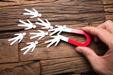 cropped image of businessman's hand holding magnet towards papermen on wooden table