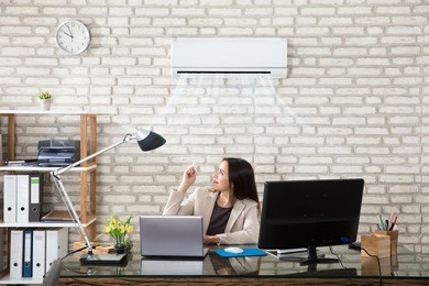 young businesswoman operating air conditioner with remote controller in office