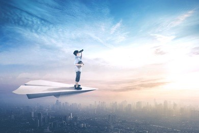 picture of little boy standing on a paper plane while flying above city and looking with binoculars