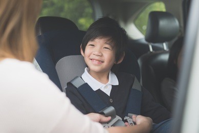 asian woman fastening child with safety seat belt in car