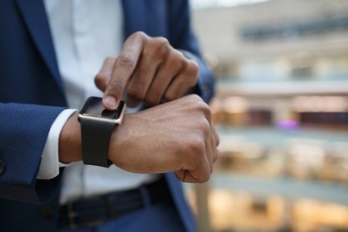 close-up of african american business  man using smart watch, standing indoors in store or office building, focus on hands, blurred background